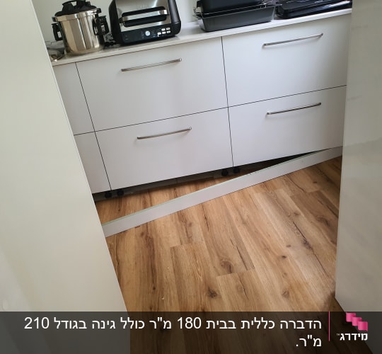 מטבח עם רצפת עץ, ארונות לבנים ומכשירי חשמל.